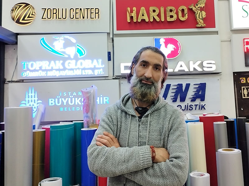 Ürettiği tabelaların önünde